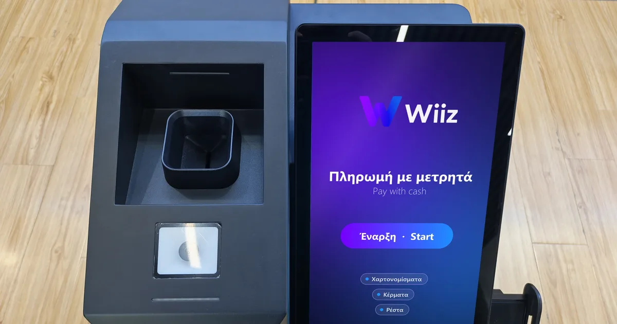 Αυτόματο ταμείο μετρητών Wiiz από ψηλά, με την οθόνη αφής να δείχνει «Πληρωμή με μετρητά»
